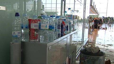 Dos viajeros esperan junto a una papelera desbordada